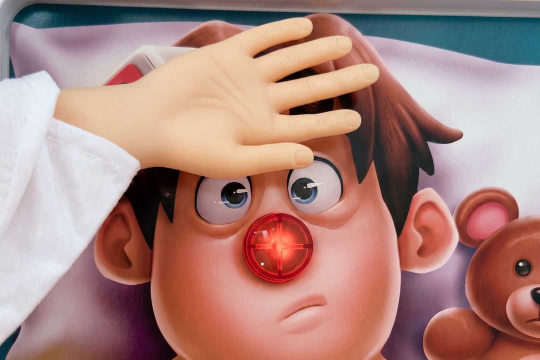 A tiny hand rests on the forehead of the patient from the board game Operation, his red nose lit up