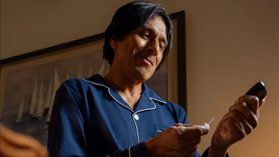 Man in navy pajamas sitting on the edge of his bed at night, smiling as he checks his blood sugar with a Contour meter and test strip.