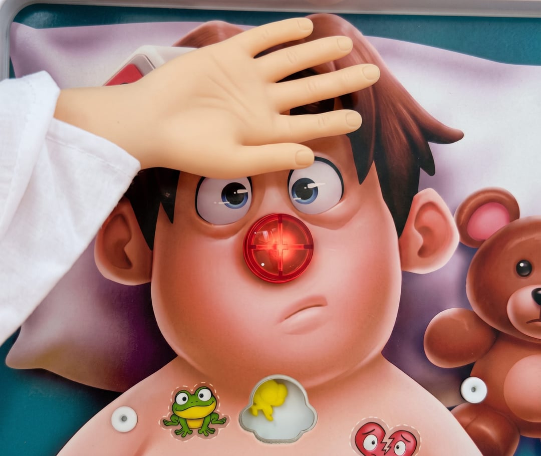 A tiny hand rests on the forehead of the patient from the board game Operation, his red nose lit up
